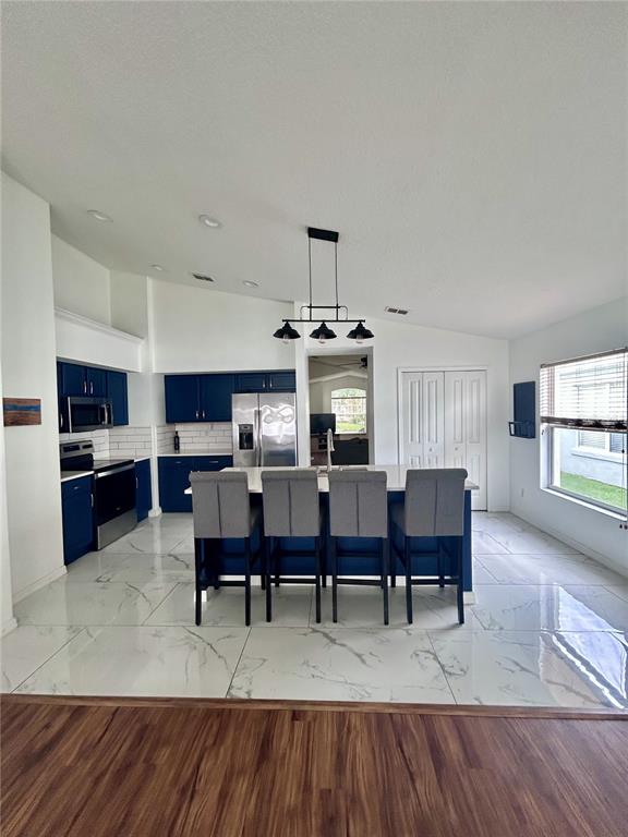 A kitchen features dark blue cabinets, a white island with bar seating, and marble-patterned flooring — 1061 PORTMOOR WAY, WINTER GARDEN, FL
