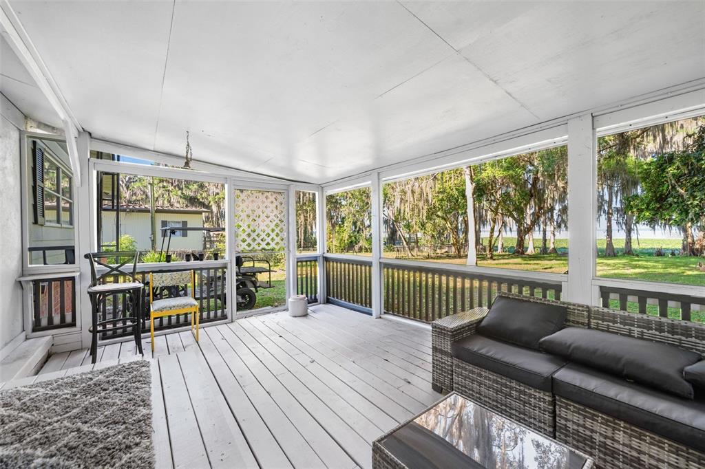 A screened-in porch with white wooden flooring, a gray sofa, and views of trees outside — 15026 SE US HIGHWAY 301, HAWTHORNE, FL