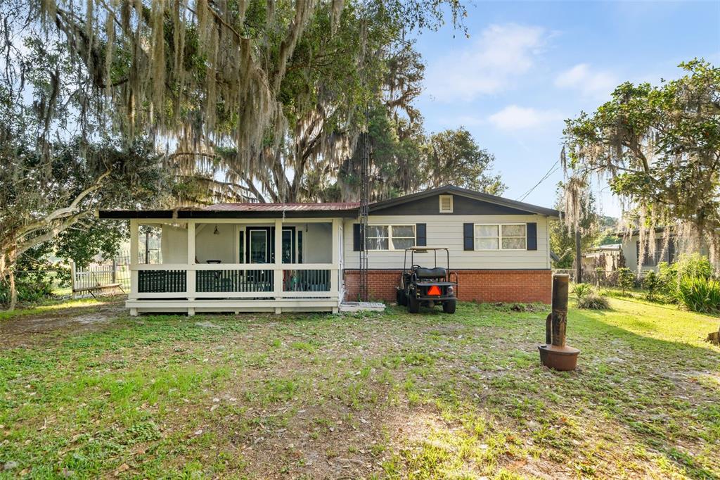 A single-story house with a screened porch, brick base, and siding under large oak trees — 15026 SE US HIGHWAY 301, HAWTHORNE, FL