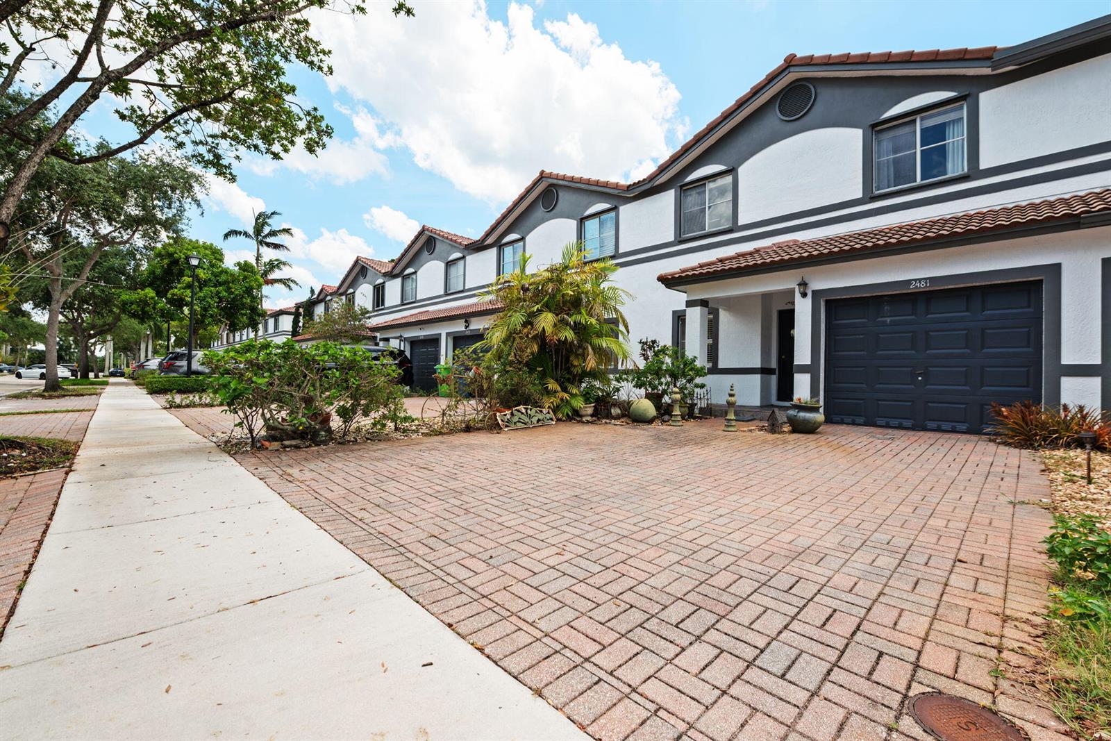 A row of two-story townhomes features white stucco walls, dark trim, and brick-paved driveways — 2481 NW 98th Lane, Sunrise FL 33322, SUNRISE, FL