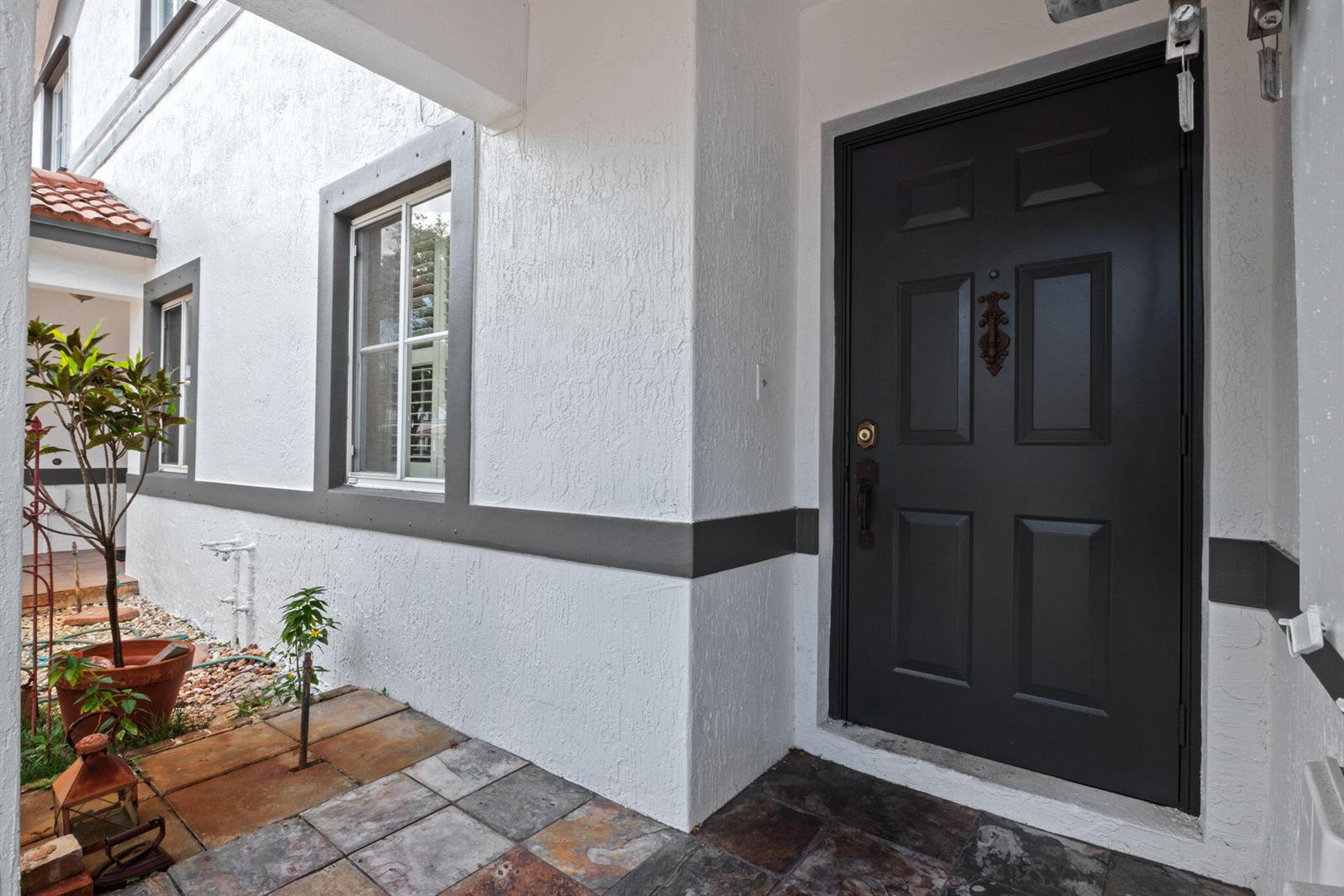 A dark front door with a knocker sits beside a window on a tiled porch — 2481 NW 98th Lane, Sunrise FL 33322, SUNRISE, FL