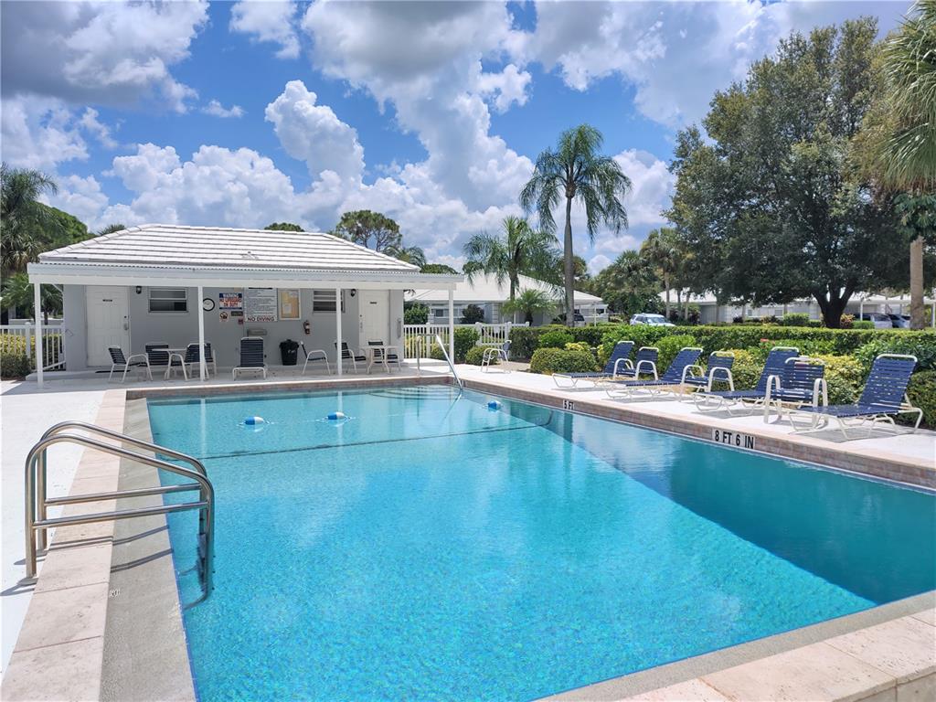 A rectangular swimming pool with lounge chairs sits in front of a small clubhouse building — 276 CERROMAR WAY S UNIT 60, VENICE, FL