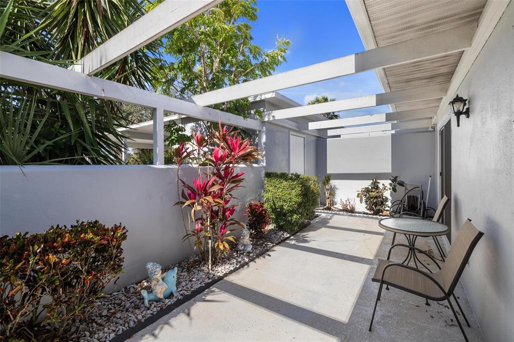 A concrete patio features a white pergola, a low privacy wall, and outdoor seating — 276 CERROMAR WAY S UNIT 60, VENICE, FL