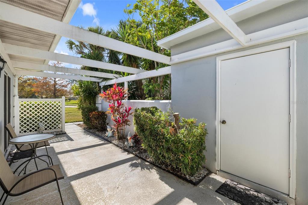 A concrete patio features a white pergola, a storage door, and a small seating area — 276 CERROMAR WAY S UNIT 60, VENICE, FL