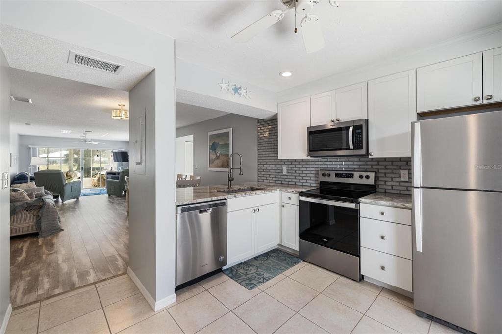 A kitchen with white cabinets, stainless steel appliances, and a gray tiled backsplash — 276 CERROMAR WAY S UNIT 60, VENICE, FL
