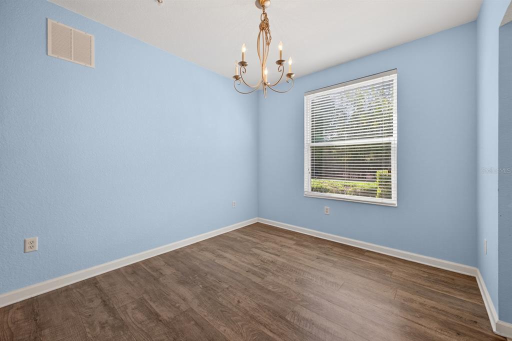An empty room with light blue walls, wood-look flooring, and a decorative chandelier — 8352 QUIMBY CIRCLE, DAVENPORT, FL