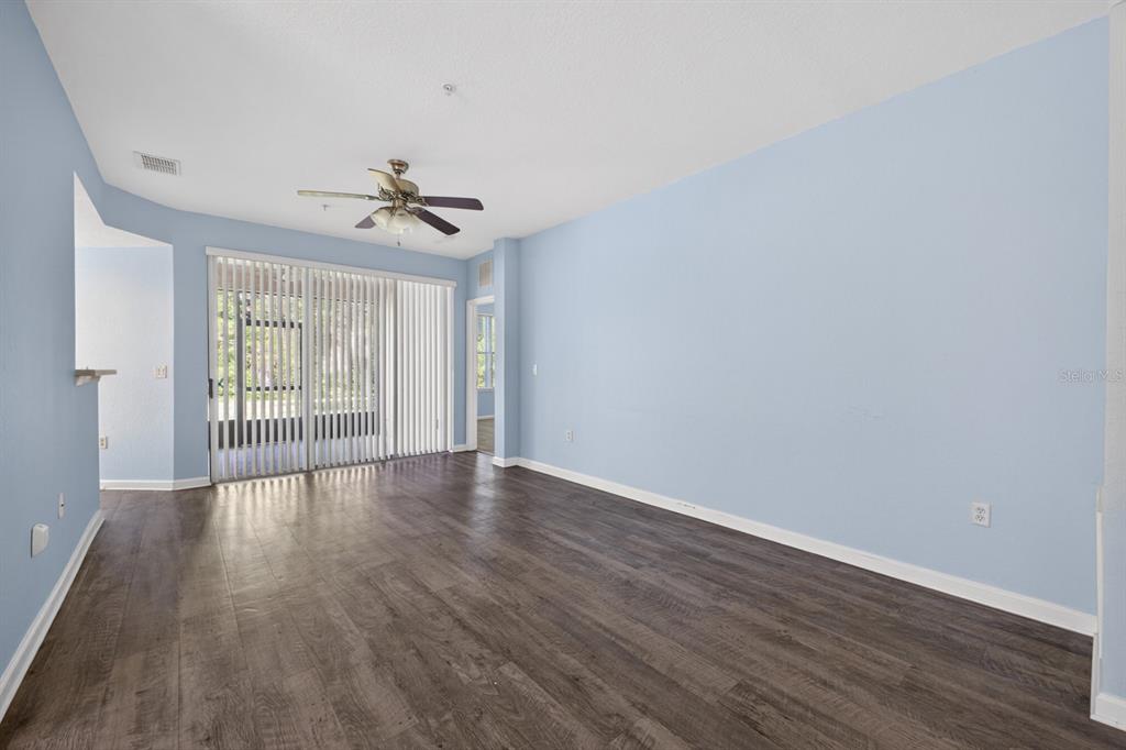 An empty living room features light blue walls, dark wood-look flooring, and a sliding glass door — 8352 QUIMBY CIRCLE, DAVENPORT, FL
