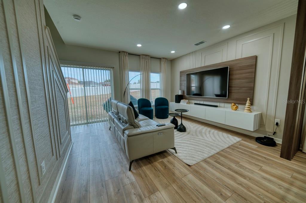 A modern living room features a wall-mounted television, light wood flooring, and a gray sofa — 1568 MIRABELLA CIRCLE, DAVENPORT, FL