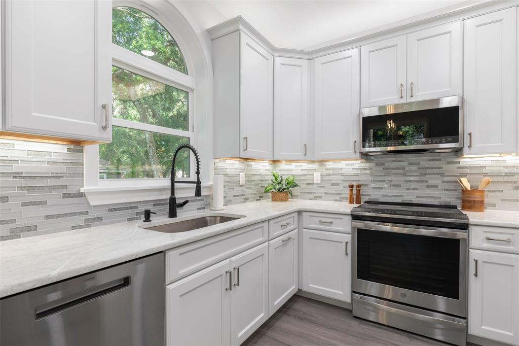 A kitchen features white cabinets, stainless steel appliances, a tile backsplash, and a corner window — 117 HERNANDEZ AVENUE, PALM COAST, FL