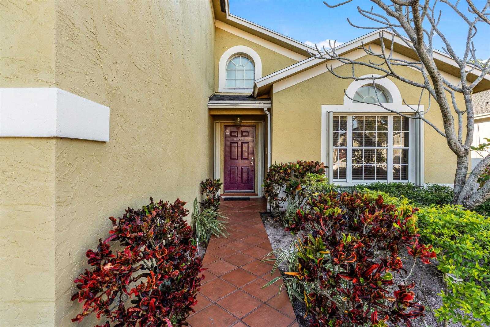 A front entrance with a purple door, tiled walkway, and colorful landscaping under a blue sky — 2224 Soundings Court, FL 33413, FL