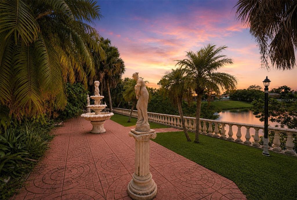A stone statue and tiered fountain sit on a paved patio overlooking a waterfront lawn — 126 ORTIZ BOULEVARD, NORTH PORT, FL