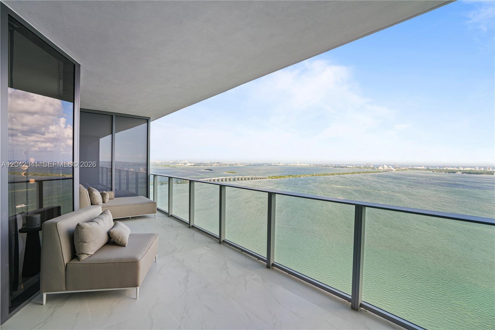 A balcony with light-colored lounge furniture overlooks a large body of water and a bridge — 700 NE 24 # 3905, Miami FL 33137, MIAMI, FL