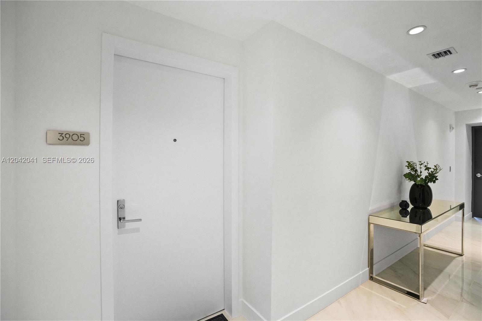 A white door with a room number sign sits beside a mirrored console table — 700 NE 24 # 3905, Miami FL 33137, MIAMI, FL