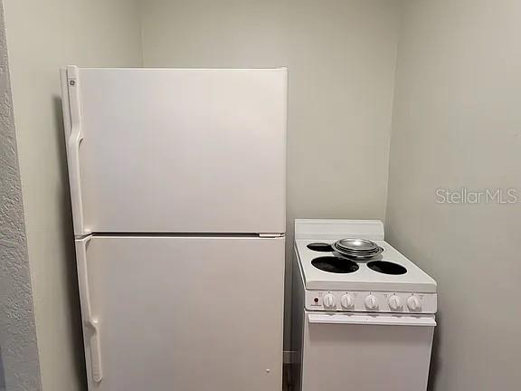 A white refrigerator stands next to a small white electric stove in a corner — 820 8TH AVENUE S UNIT E, ST PETERSBURG, FL
