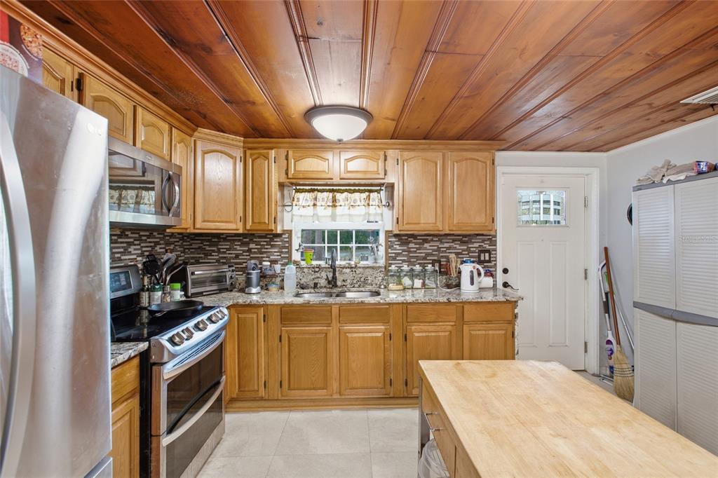 A kitchen with wood-paneled ceilings, oak cabinets, granite countertops, and a wooden kitchen island — 40832 RIVER ROAD, DADE CITY, FL