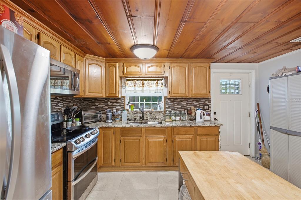 A kitchen features wood-paneled ceilings, oak cabinetry, granite countertops, and a central wooden island — 40832 RIVER ROAD, DADE CITY, FL