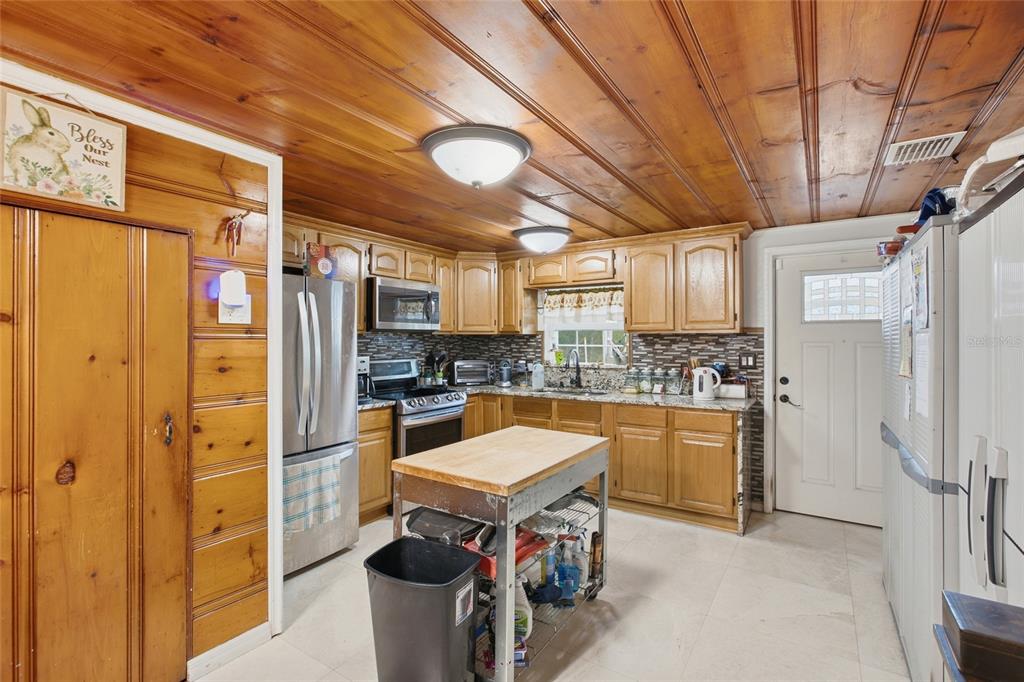 This kitchen features wood-paneled walls and ceilings, oak cabinets, granite countertops, and a rolling island — 40832 RIVER ROAD, DADE CITY, FL