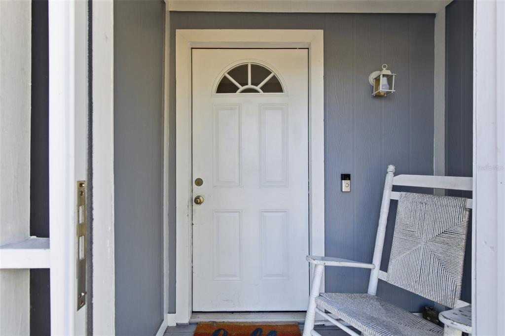 A white front door with a semi-circular window sits on a porch with a rocking chair — 3706 NW 1ST TERRACE, CAPE CORAL, FL