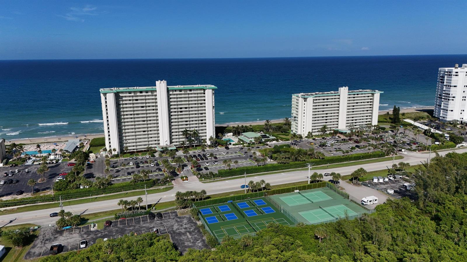 An aerial view shows two high-rise apartment buildings near the ocean with tennis courts nearby — 9940 S Ocean Drive # 1005, Jensen Beach FL 34957, JENSEN BEACH, FL