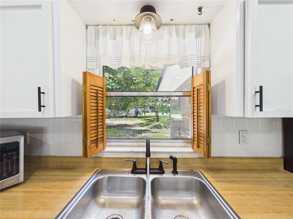 A kitchen sink with a wooden countertop sits beneath a window with wooden shutters — 6155 NW 58TH TERRACE, OCALA, FL