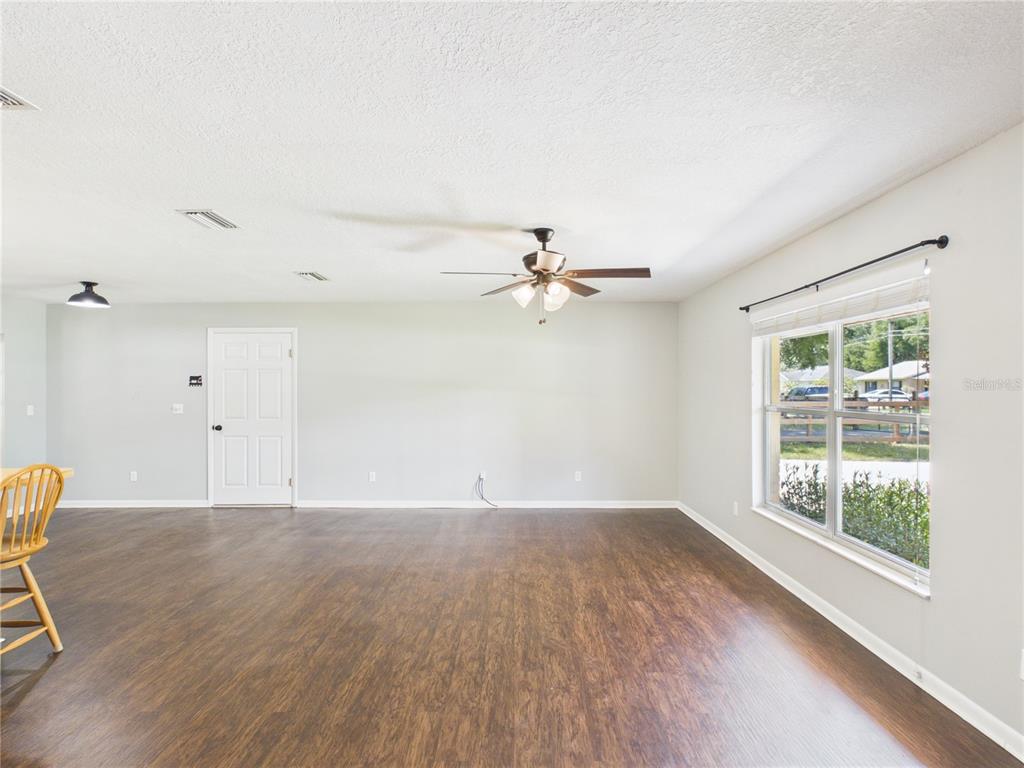 An empty room features dark wood-look flooring, light gray walls, a ceiling fan, and a window — 6155 NW 58TH TERRACE, OCALA, FL