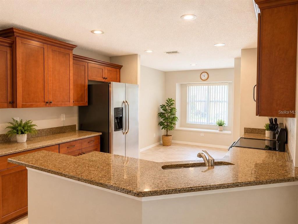 A kitchen with granite countertops, wooden cabinets, and a stainless steel refrigerator overlooks a dining area — 822 MCCALLISTER UNIT 822, SUN CITY CENTER, FL