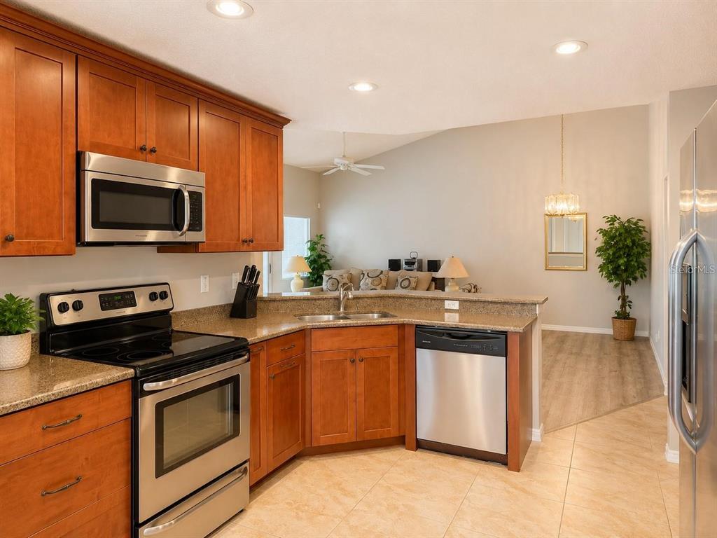 A kitchen with wood cabinets, stainless steel appliances, and granite countertops overlooks a living area — 822 MCCALLISTER UNIT 822, SUN CITY CENTER, FL