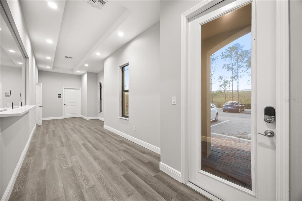 A bright, modern interior hallway features light wood-look flooring, recessed lighting, and a glass-paneled door — 4347 HUNTERS PARK LANE UNIT 102, ORLANDO, FL