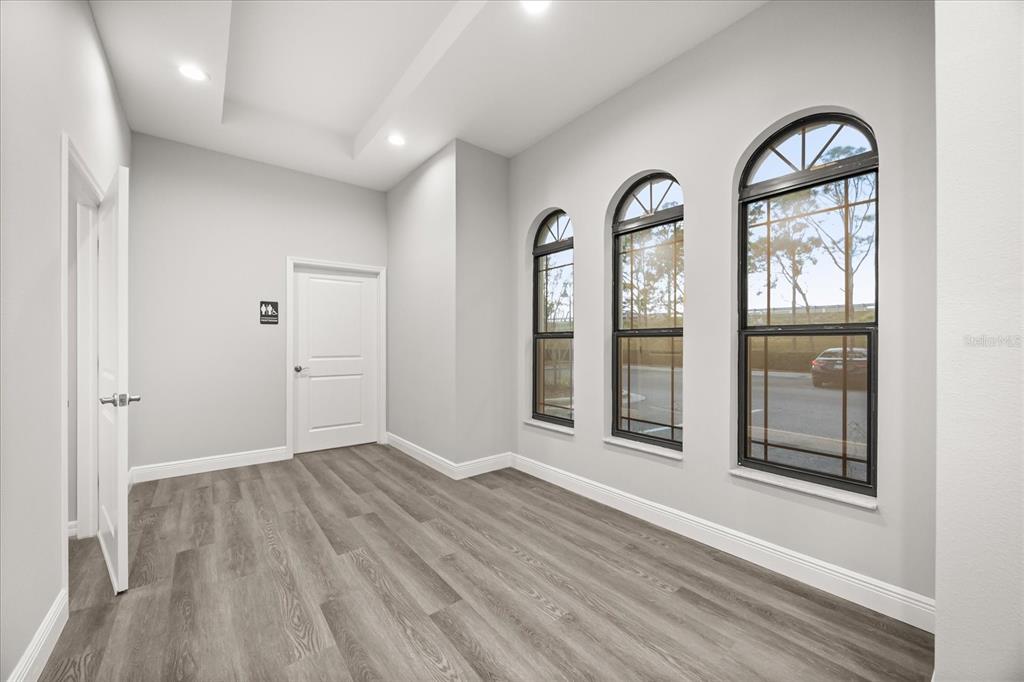 An empty room with gray wood-look flooring, white walls, and three arched windows — 4347 HUNTERS PARK LANE UNIT 102, ORLANDO, FL