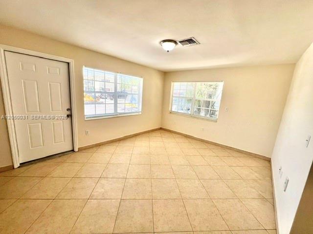 An empty room features beige tile flooring, white walls, two windows, and a white door — 696 NE 85th St # 1, Miami FL 33138, MIAMI, FL