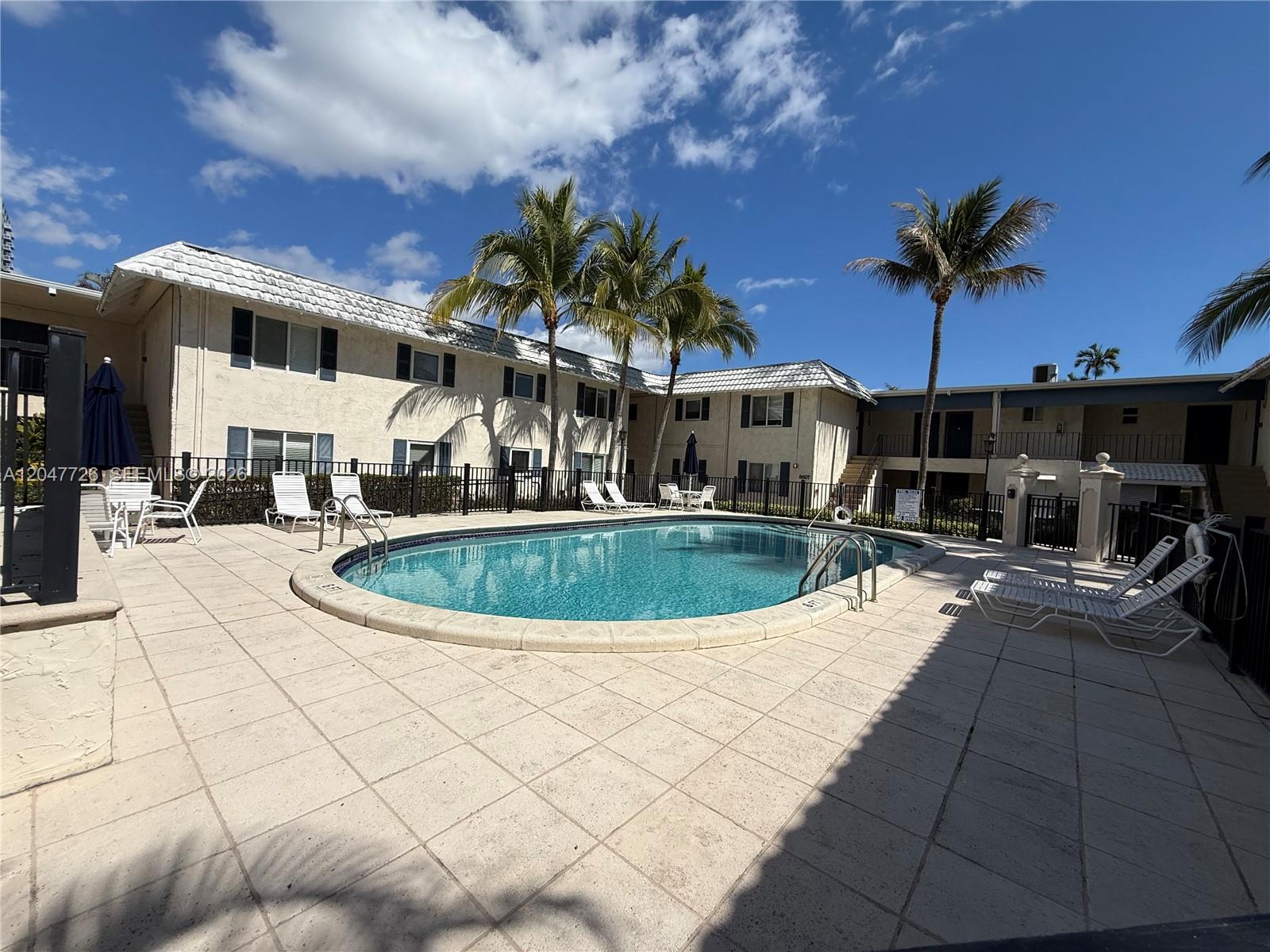 A swimming pool sits in a paved courtyard surrounded by two-story apartment buildings and palms — 8607 SW 68th Ct # 24, Pinecrest FL 33156, PINECREST, FL