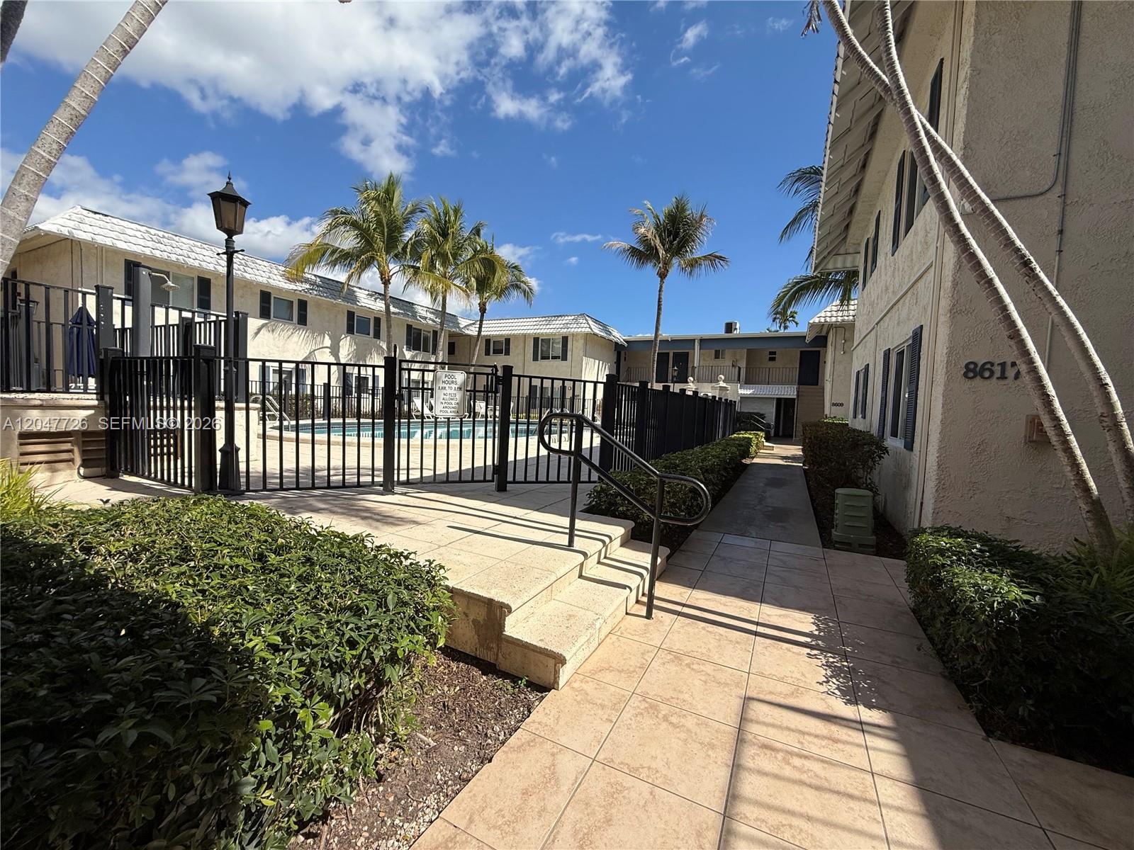A swimming pool area is enclosed by a black metal fence near a residential building — 8607 SW 68th Ct # 24, Pinecrest FL 33156, PINECREST, FL