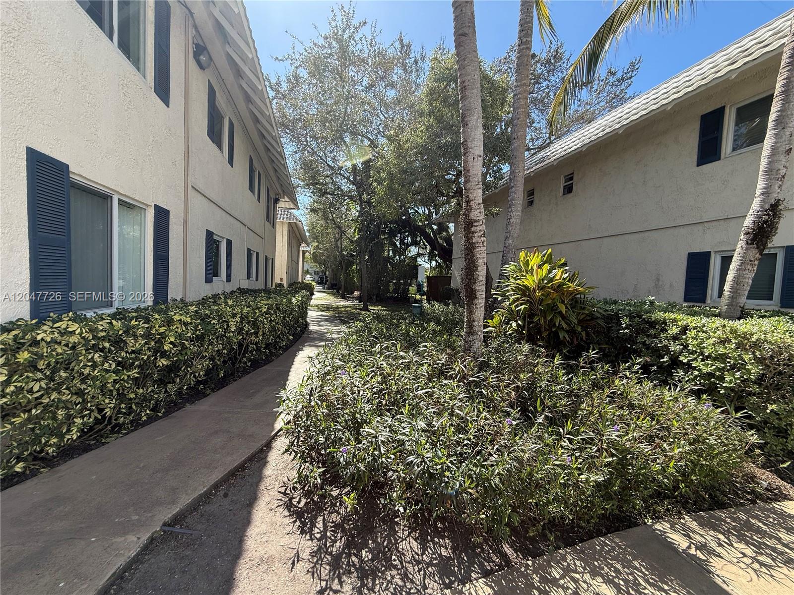 A concrete walkway leads between two multi-story residential buildings surrounded by lush landscaping and trees — 8607 SW 68th Ct # 24, Pinecrest FL 33156, PINECREST, FL