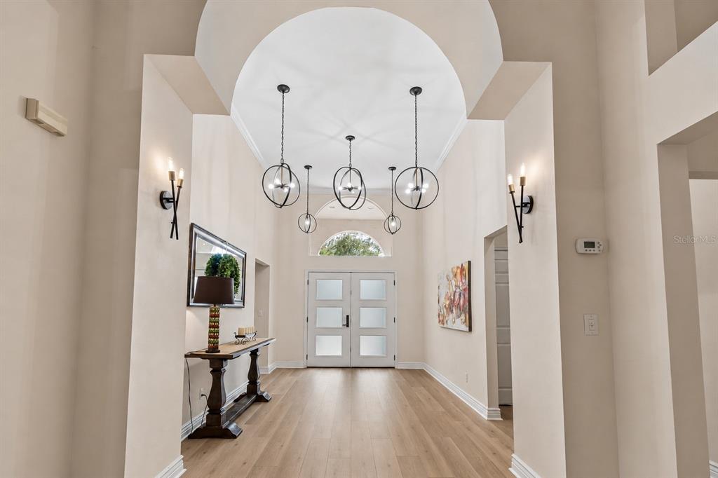 A bright foyer features light wood flooring, a high arched ceiling, and three globe chandeliers — 17503 EDINBURGH DRIVE, TAMPA, FL