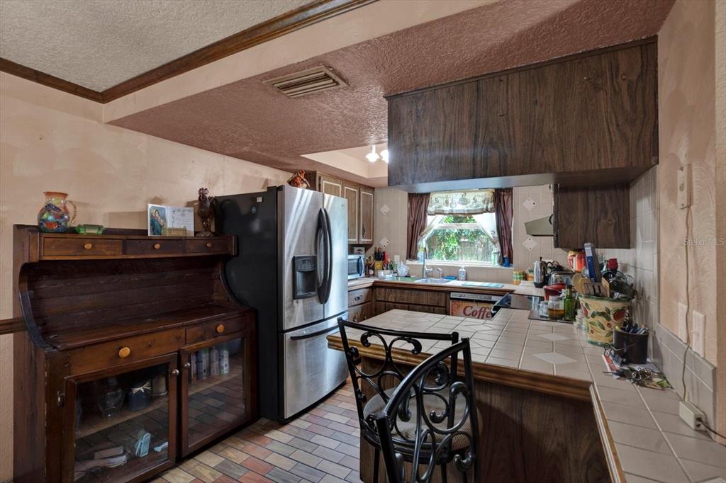 A kitchen features a tiled peninsula, stainless steel refrigerator, and dark wood cabinetry — 12030 106TH COURT, LARGO, FL