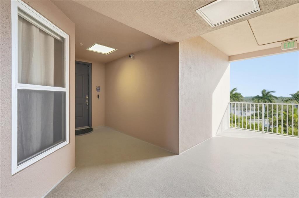 An outdoor balcony features a gray door, a white railing, and a view of trees — 395 ARUBA CIRCLE UNIT 303, BRADENTON, FL