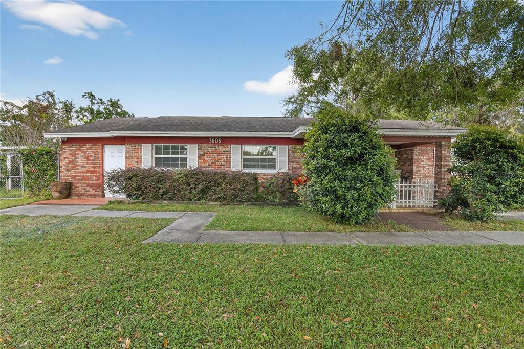 A single-story brick house with a front porch, lawn, and sidewalk under a blue sky — 3605 W FLORA STREET, TAMPA, FL