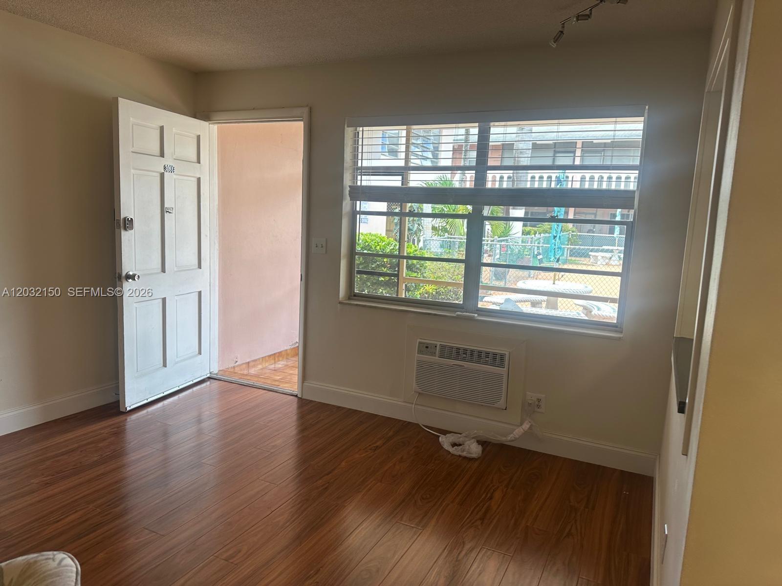 A room with wood-look flooring, a white door, a window with blinds, and an air conditioner — 160 NE 8th Ave # 25A, Hallandale Beach FL 33009, HALLANDALE BEACH, FL