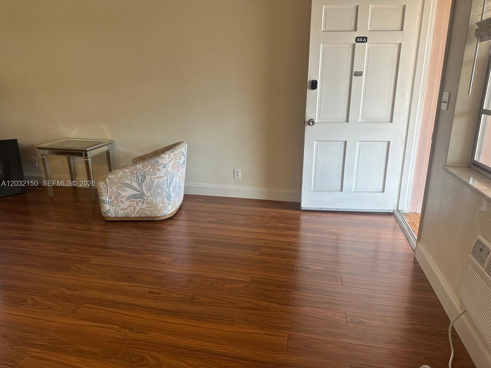 A room with wood-look flooring, a patterned armchair, a mirrored side table, and a door — 160 NE 8th Ave # 25A, Hallandale Beach FL 33009, HALLANDALE BEACH, FL