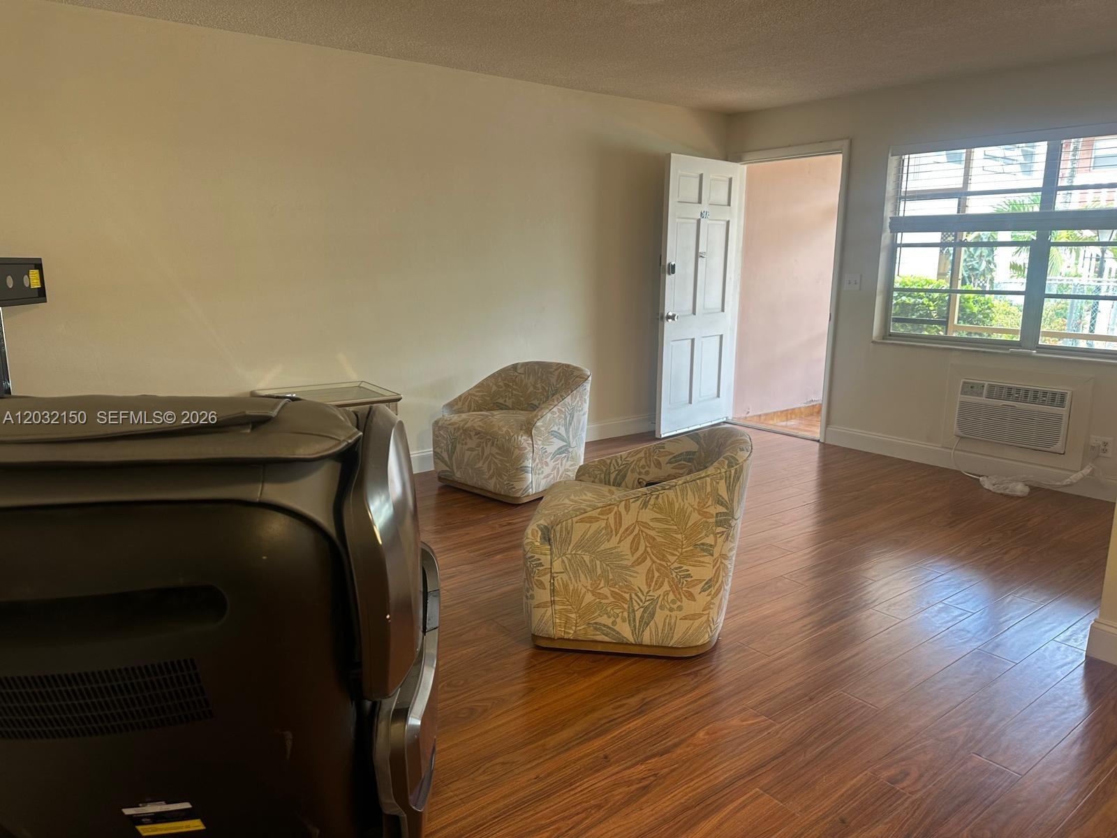 A living room features wood-look flooring, two patterned armchairs, and an open exterior door — 160 NE 8th Ave # 25A, Hallandale Beach FL 33009, HALLANDALE BEACH, FL