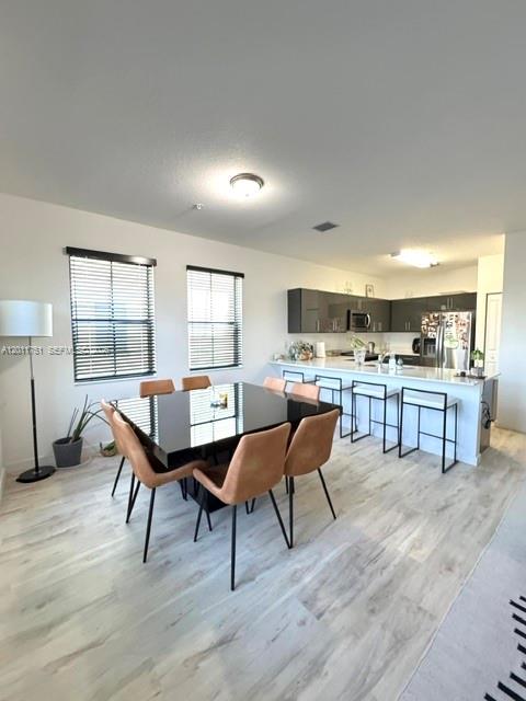 A modern open-concept dining area and kitchen feature light wood flooring and dark cabinetry — 15650 SW 136th St # 101, Miami FL 33196, MIAMI, FL
