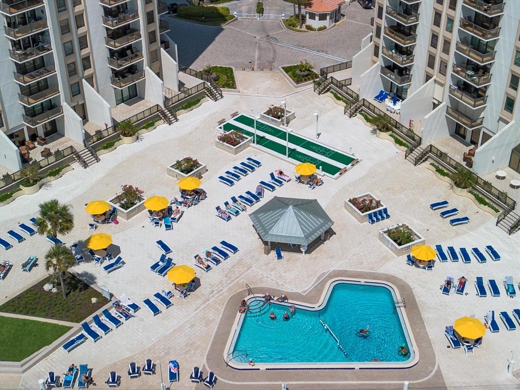 An aerial view shows a swimming pool, shuffleboard court, and lounge chairs between two buildings — 450 S GULFVIEW BOULEVARD UNIT 1204, CLEARWATER, FL