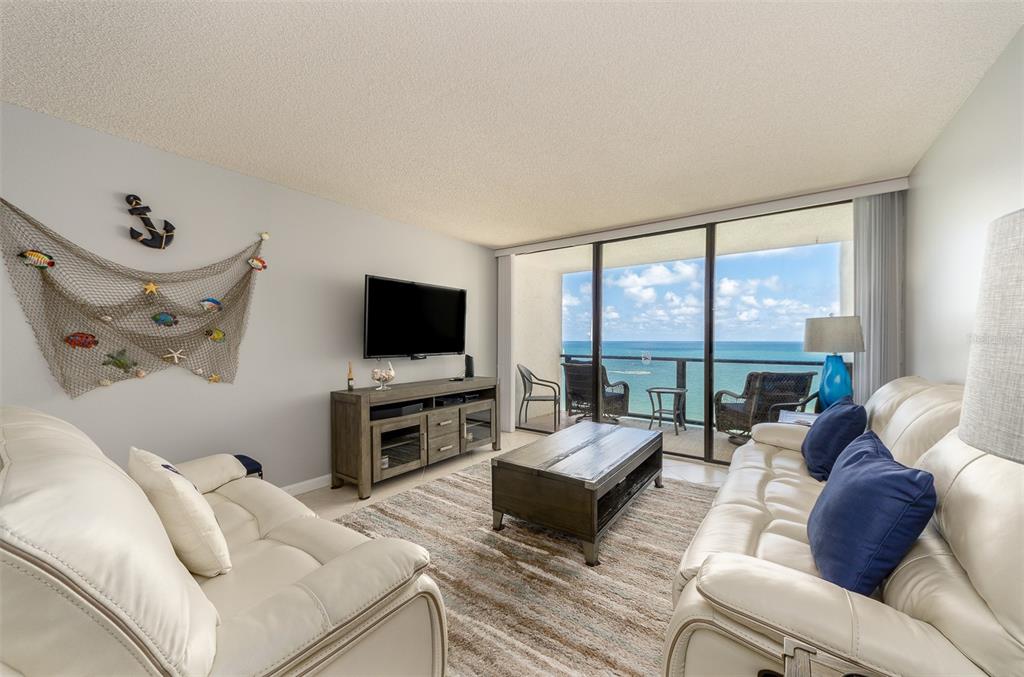 A living room features white leather sofas, a wooden media console, and a balcony overlooking the ocean — 450 S GULFVIEW BOULEVARD UNIT 1204, CLEARWATER, FL