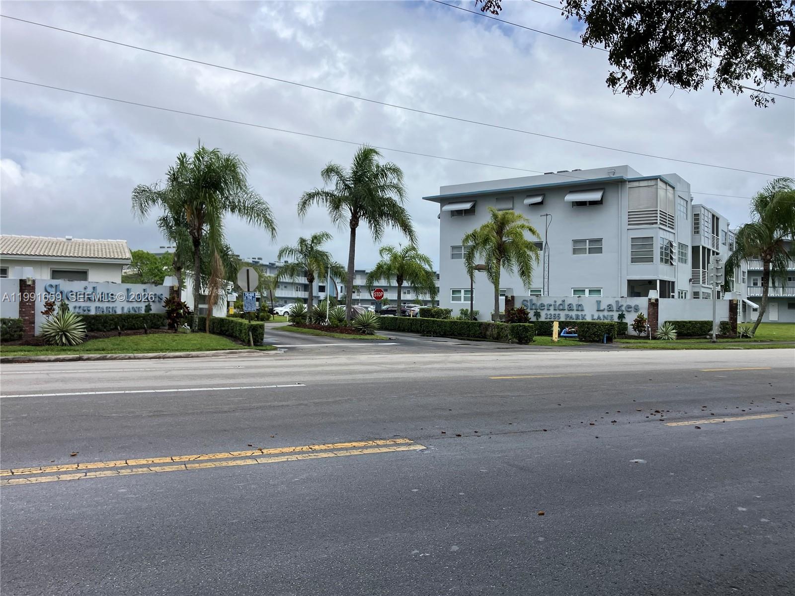 The exterior of a multi-story apartment complex features palm trees and a gated entrance — 2300 Park Ln # 203, Hollywood FL 33021, HOLLYWOOD, FL