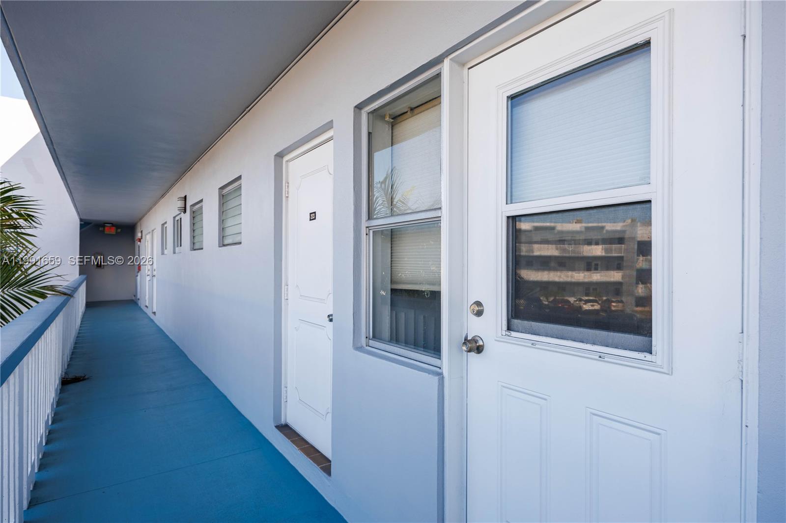 An outdoor walkway with blue flooring leads past several white doors and windows — 2300 Park Ln # 203, Hollywood FL 33021, HOLLYWOOD, FL