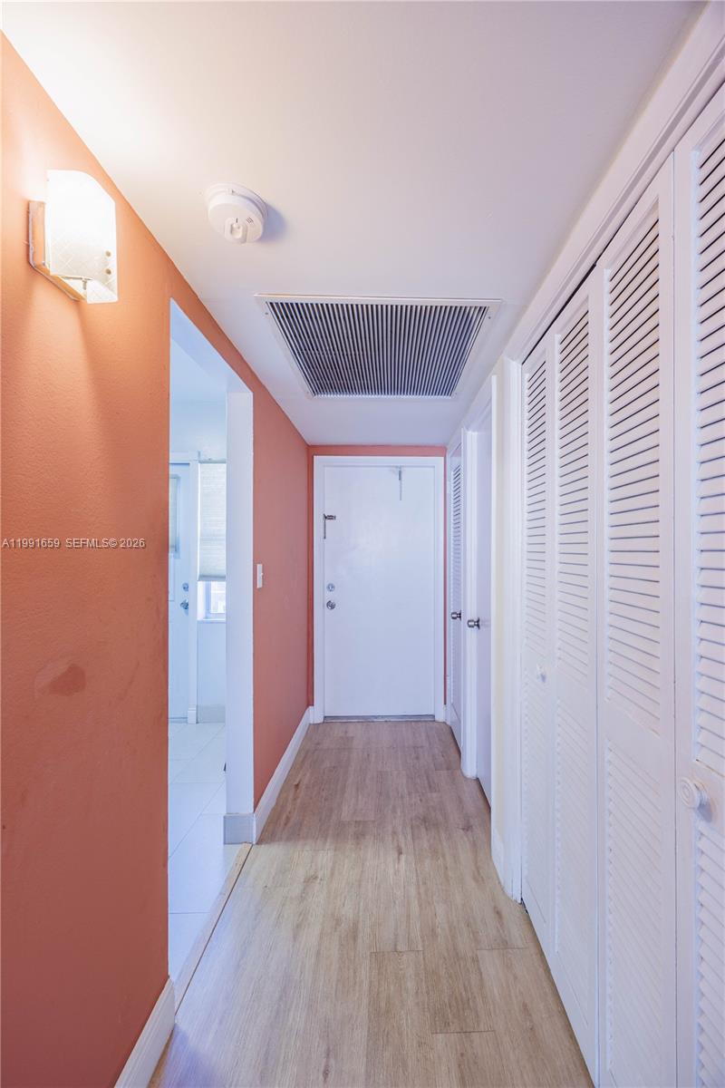 A hallway features wood-look flooring, peach-colored walls, a ceiling vent, and white louvered closet doors — 2300 Park Ln # 203, Hollywood FL 33021, HOLLYWOOD, FL