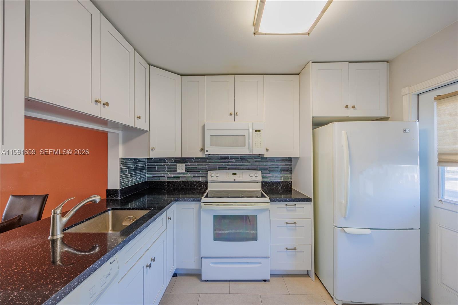 A kitchen features white cabinets, black countertops, a glass tile backsplash, and white appliances — 2300 Park Ln # 203, Hollywood FL 33021, HOLLYWOOD, FL