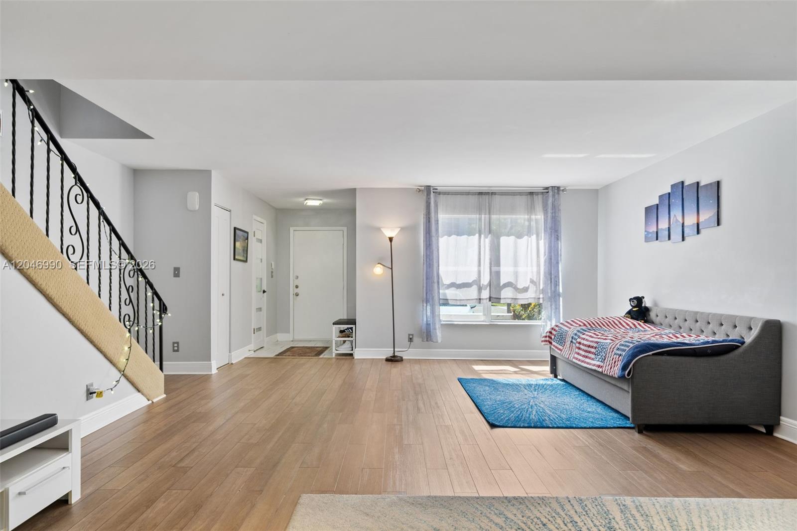 A living room features wood-look flooring, a staircase with a black railing, and a daybed — 801 NE 27th Ave, Hallandale Beach FL 33009, HALLANDALE BEACH, FL