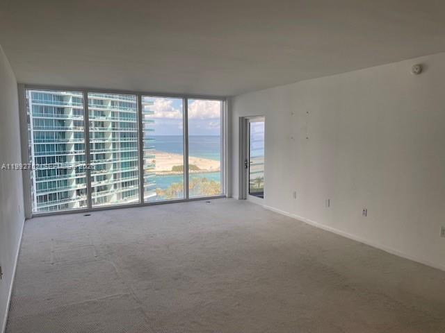 An empty living room features beige carpeting, white walls, and floor-to-ceiling windows overlooking the ocean — 10275 Collins Ave # 1107, Bal Harbour FL 33154, BAL HARBOUR, FL