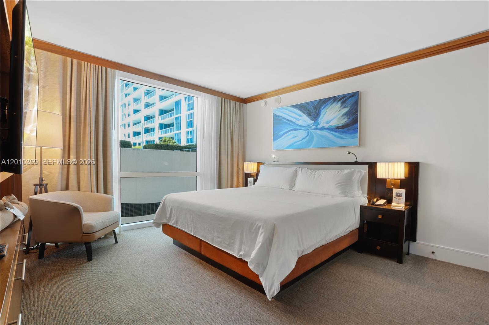 A hotel-style bedroom features a king bed, a beige armchair, and a large window — 6801 Collins Ave # 503, Miami Beach FL 33141, MIAMI BEACH, FL